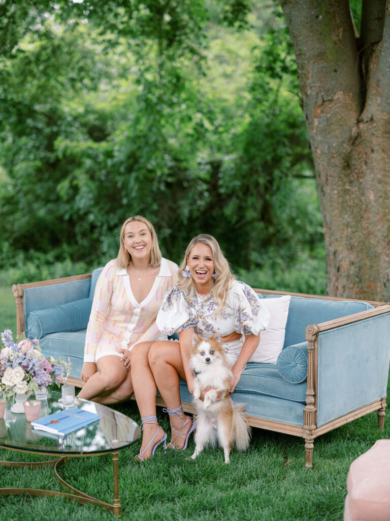 Two women sitting on a vintage couch with a dog